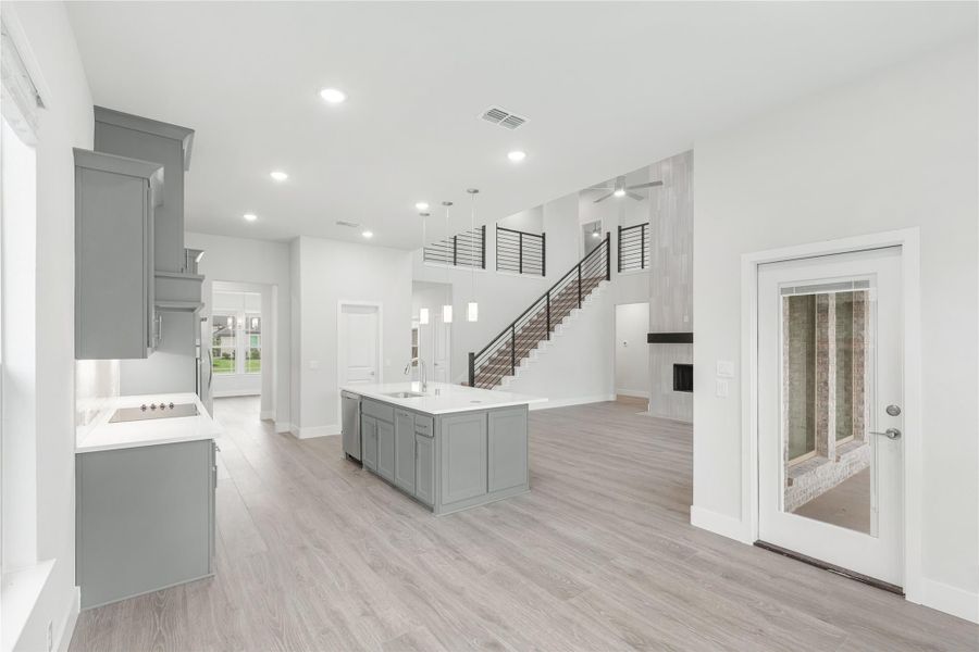 Open-concept kitchen with gray cabinets, center island, and staircase visible in background on light wood floors