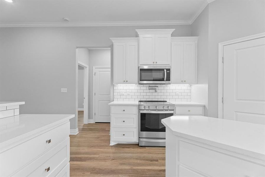 Kitchen featuring appliances with stainless steel finishes, tasteful backsplash, white cabinetry, light wood-style flooring, and light stone countertops