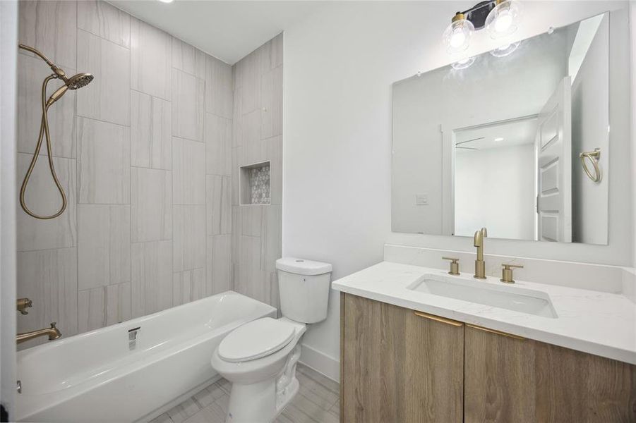 Secondary bathroom on third floor features sleek cabinetry, white countertops, gold-tone fixtures. A combination tub and shower with tile surround and built-in niche for toiletries complete the space.