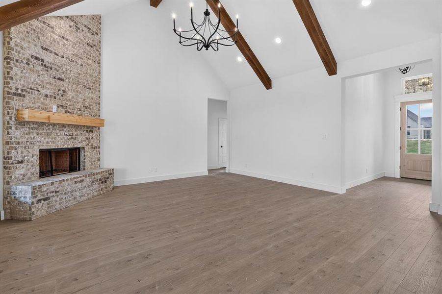 Spacious interior featuring a brick fireplace with a wood mantle, vaulted ceiling with exposed wood beams, and a black chandelier Spacious interior featuring a brick fireplace with a wood mantle, vaulted ceiling with exposed wood beams, and a black chandelier