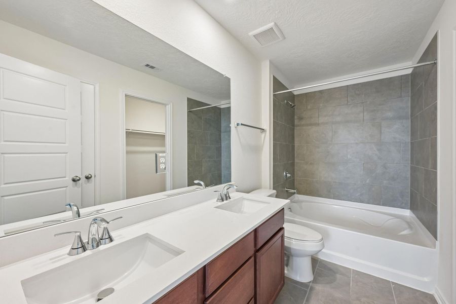 This stunning primary bathroom is truly move-in ready! It features tub/shower combination with tile surround, stained cabinetry with light countertops, dual sinks, a large mirror, high ceilings, custom paint, a large window, and sleek modern finishes throughout.