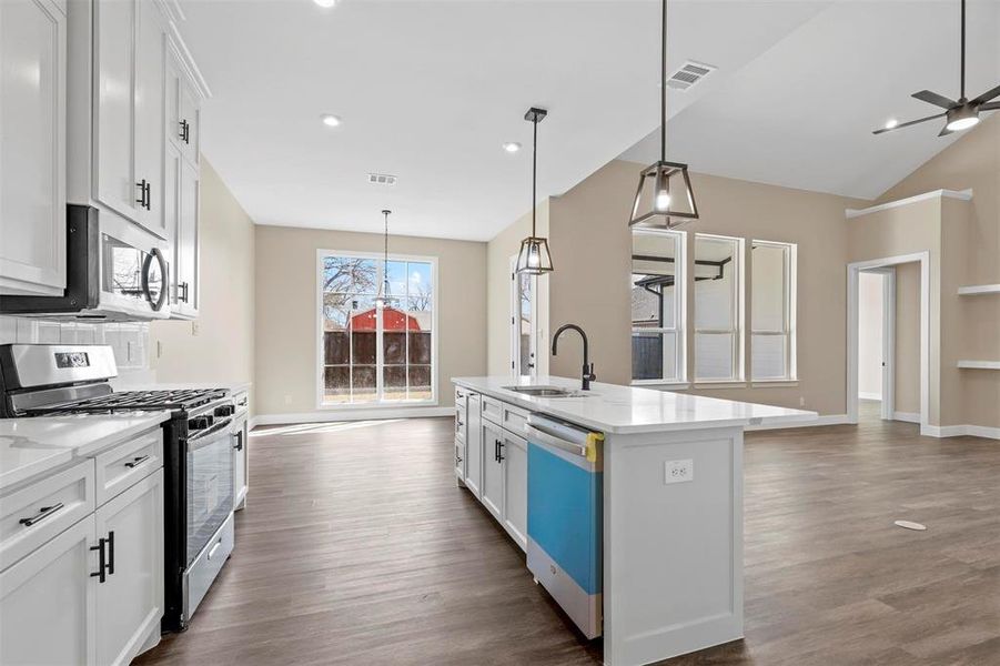 Kitchen with appliances with stainless steel finishes, sink, pendant lighting, white cabinets, and a kitchen island with sink