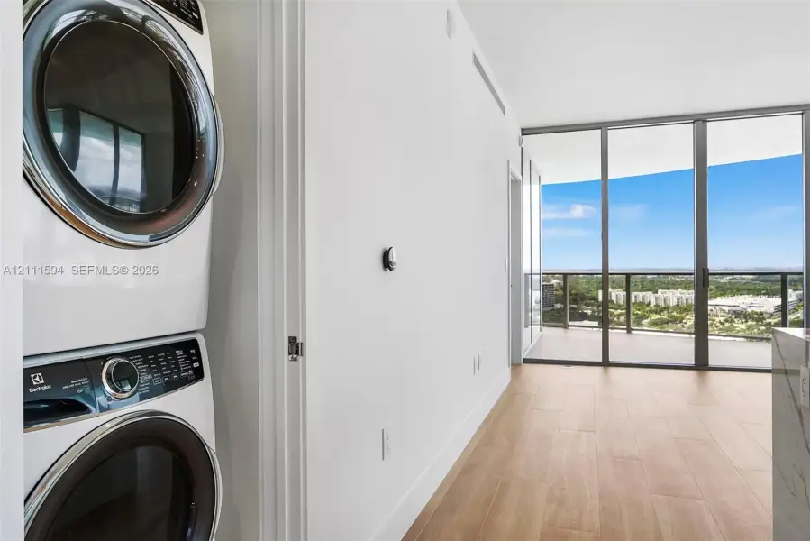 Stacked laundry appliances, wood-finish flooring, floor-to-ceiling windows, and private balcony Stacked laundry appliances, wood-finish flooring, floor-to-ceiling windows, and private balcony