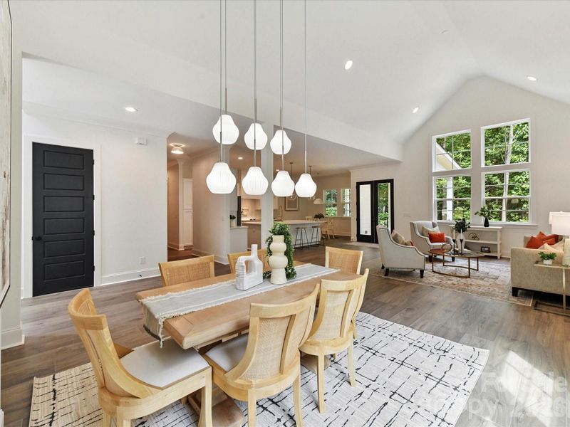 Luminous dining area with vaulted ceilings, large windows overlooking the wooded yard, and modern pendant lighting creating an inviting space for gatherings.