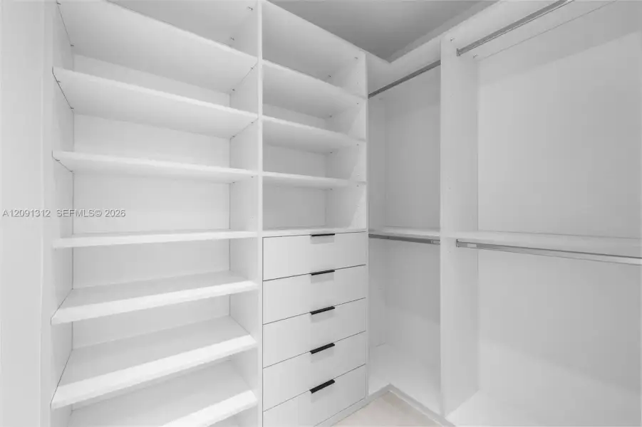 Custom walk-in closet featuring white built-in shelving, a five-drawer dresser unit, integrated hanging rods, and matte black hardware Custom walk-in closet featuring white built-in shelving, a five-drawer dresser unit, integrated hanging rods, and matte black hardware