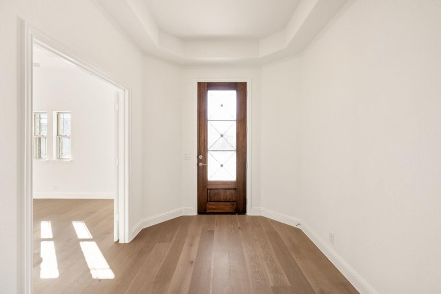 Entryway with wood front door, glass panels, tray ceiling, and light hardwood floors Entryway with wood front door, glass panels, tray ceiling, and light hardwood floors