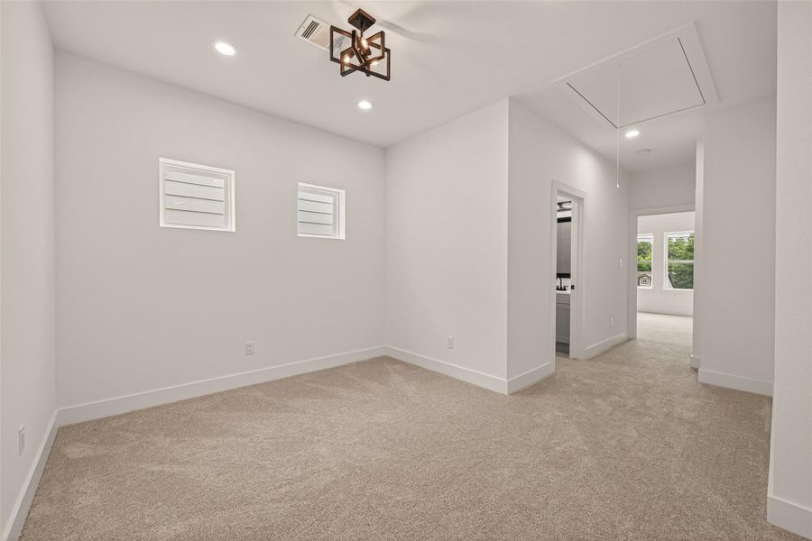 This photo shows a bright, carpeted room with modern lighting, featuring two small windows. The room leads to a hallway and has an adjacent space visible, suggesting an open layout. This photo shows a bright, carpeted room with modern lighting, featuring two small windows. The room leads to a hallway and has an adjacent space visible, suggesting an open layout.