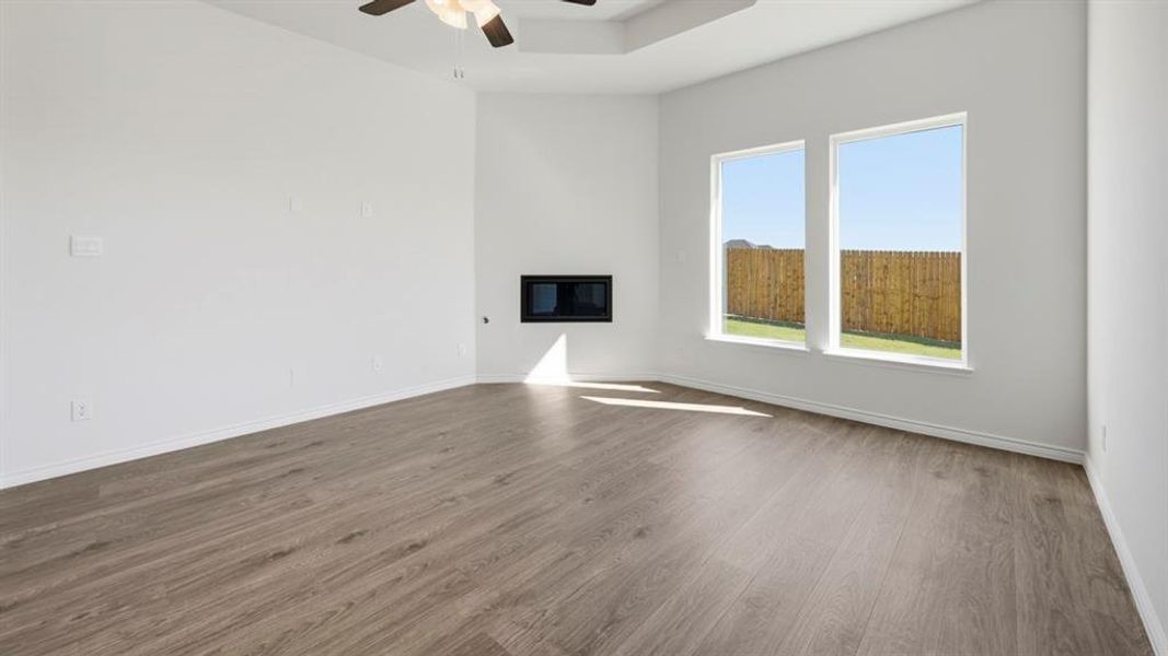 Unfurnished living room featuring a glass covered fireplace, wood finished floors, a ceiling fan, and a tray ceiling
