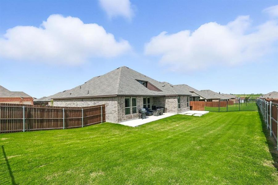 Rear view of property featuring brick siding, a patio, a fenced backyard, and roof with shingles