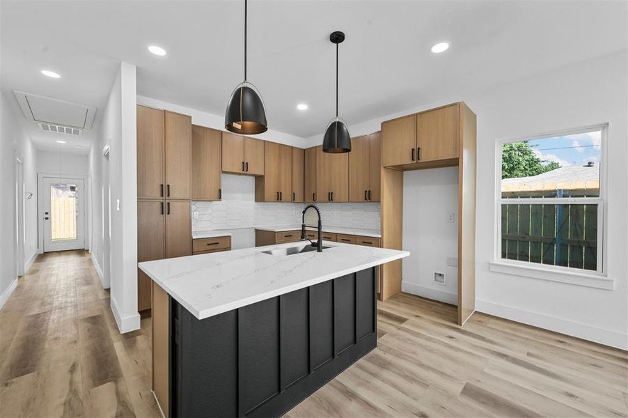 Kitchen with decorative light fixtures, light hardwood / wood-style floors, a center island with sink, tasteful backsplash, and sink