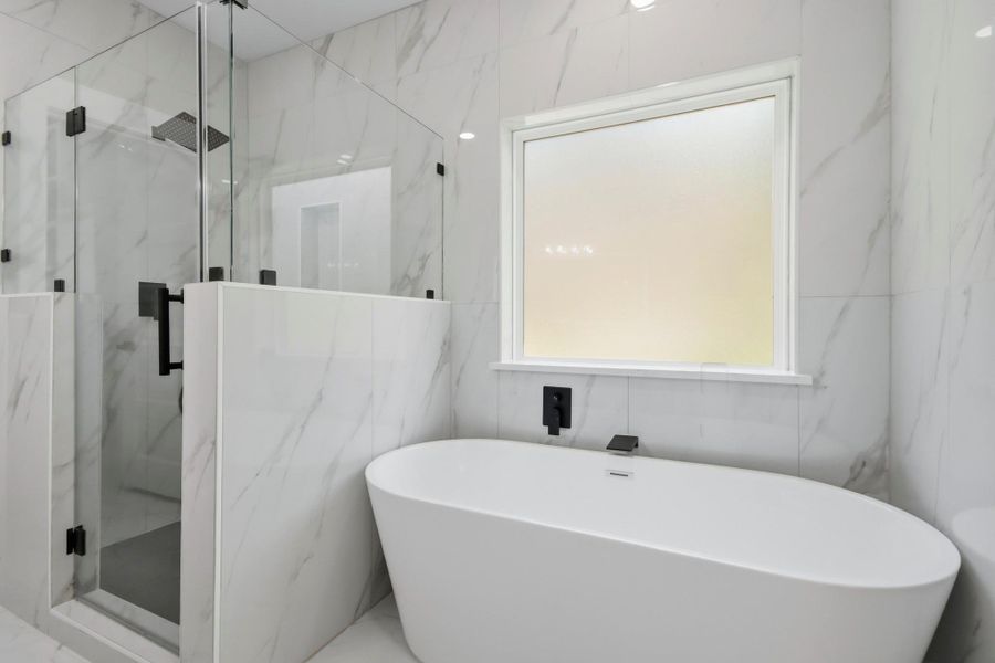 This modern oasis features a deep freestanding soaking tub under a frosted privacy window, alongside a premium glass shower with floor-to-ceiling marble-look tile and matte black fixtures. This modern oasis features a deep freestanding soaking tub under a frosted privacy window, alongside a premium glass shower with floor-to-ceiling marble-look tile and matte black fixtures.