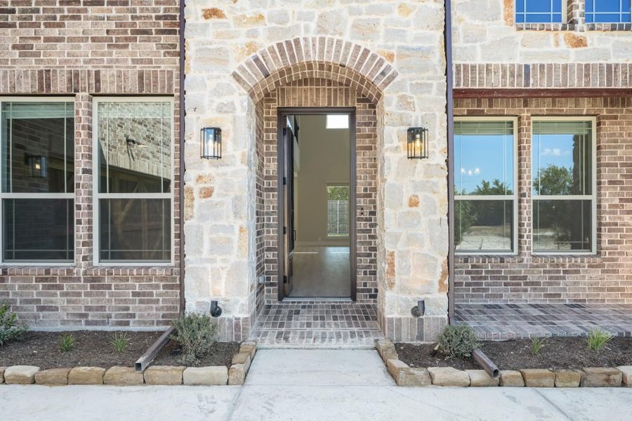Home entrance with stone arch, dark front door, brick exterior, and wall sconce lighting