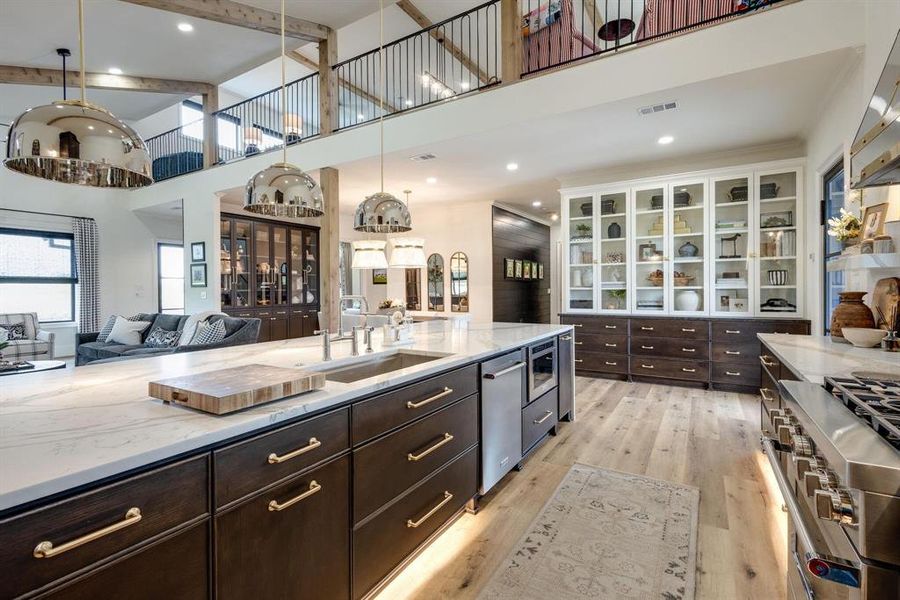 Kitchen featuring a high ceiling, white cabinets, sink, decorative light fixtures, and light hardwood / wood-style floors Kitchen featuring a high ceiling, white cabinets, sink, decorative light fixtures, and light hardwood / wood-style floors