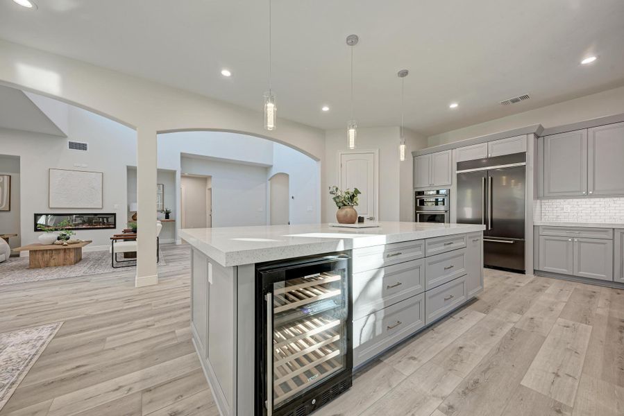 Kitchen featuring gray cabinetry, beverage cooler, pendant lighting, open floor plan, and arched walkways