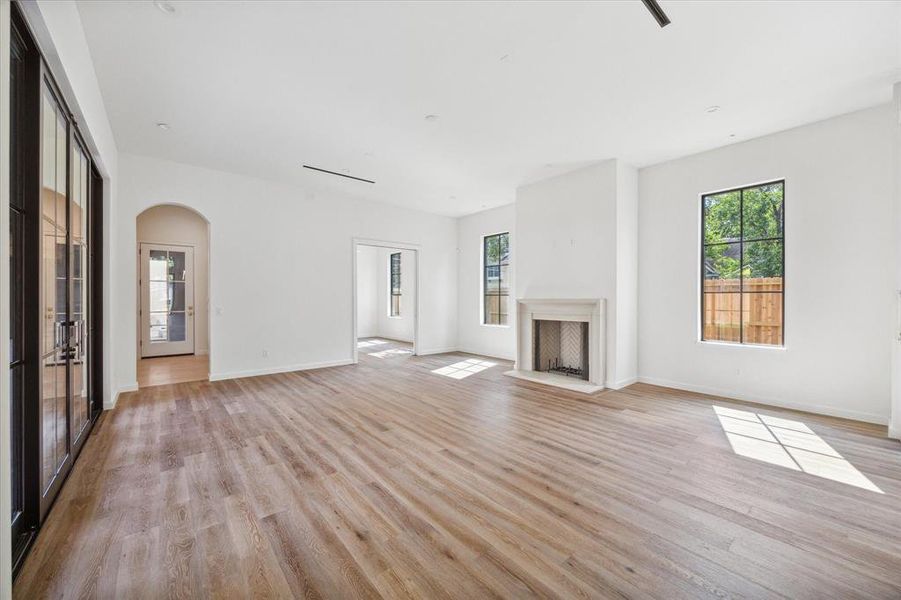 Living area with a central gas fireplace with natural stone surround, large windows offering an abundance of natural light, and sliding glass doors lead to the outdoor patio/kitchen, emphasizing the room's indoor-outdoor flow. There is also access to the back door with a drop zone that flows through the breezeway to the garage.