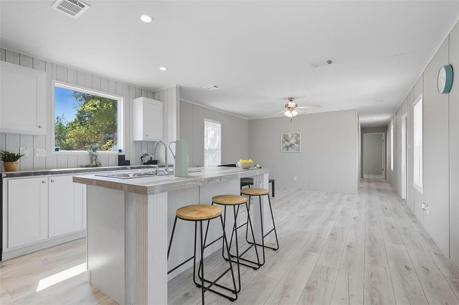 Kitchen with white cabinets, a breakfast bar area, recessed lighting, light wood-type flooring, and an island with sink Kitchen with white cabinets, a breakfast bar area, recessed lighting, light wood-type flooring, and an island with sink
