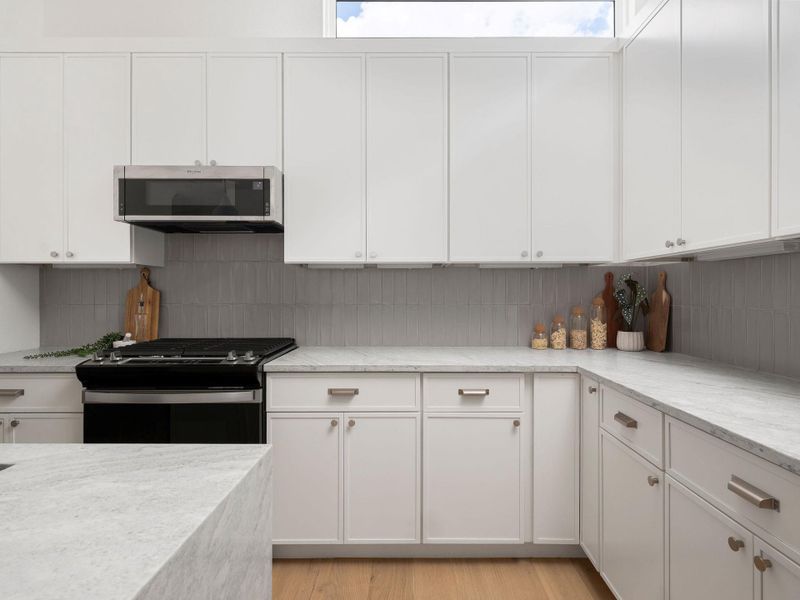 White cabinetry, light stone countertops, and natural wood flooring converge in this well-appointed kitchen.