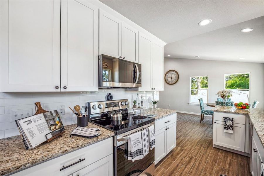 Kitchen featuring lofted ceiling, white cabinetry, stainless steel appliances, light stone countertops, and dark hardwood / wood-style flooring