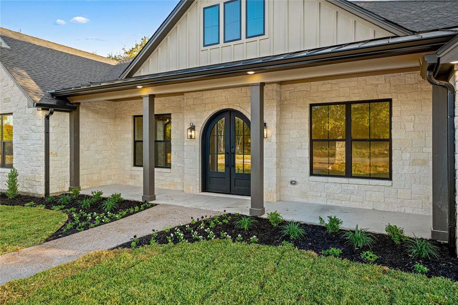 View of exterior entry featuring stone siding, covered porch, board and batten siding, and roof with shingles