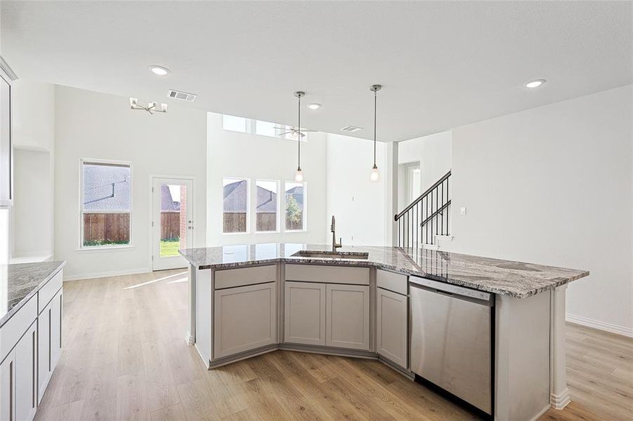 Kitchen featuring stainless steel dishwasher, sink, a kitchen island with sink, and light wood-type flooring