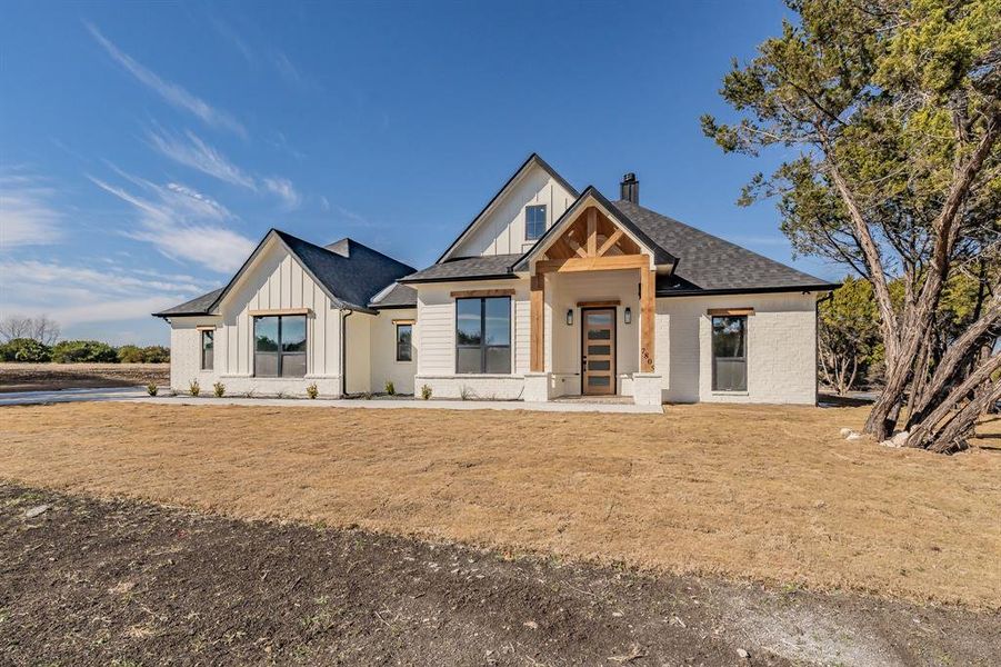 Modern inspired farmhouse with board and batten siding, a chimney, a front yard, and covered porch