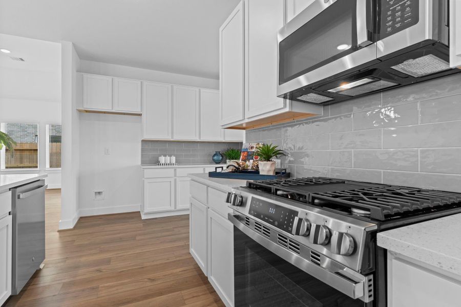 Sleek stainless steel gas range with matching built-in microwave is set against a glossy gray tile backsplash—adding a modern touch to this well-appointed kitchen. **Image Representative of Plan Only and May Vary as Built**.