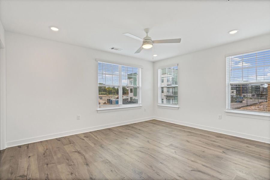 Spacious room featuring wood-finish flooring, multiple windows, recessed lighting, and a ceiling fan
