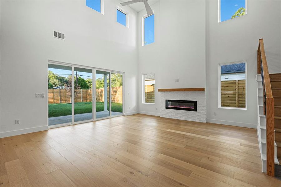 Unfurnished living room featuring light wood-style flooring, a glass covered fireplace, and a high ceiling