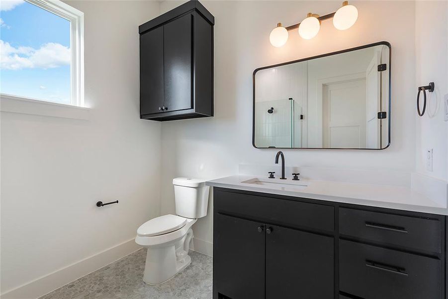 Bathroom featuring a white vanity with dark cabinetry, a rectangular framed mirror, three-light vanity fixture, and a window Bathroom featuring a white vanity with dark cabinetry, a rectangular framed mirror, three-light vanity fixture, and a window