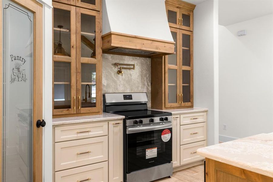 Kitchen featuring backsplash, light hardwood / wood-style flooring, stainless steel range, light stone counters, and custom range hood