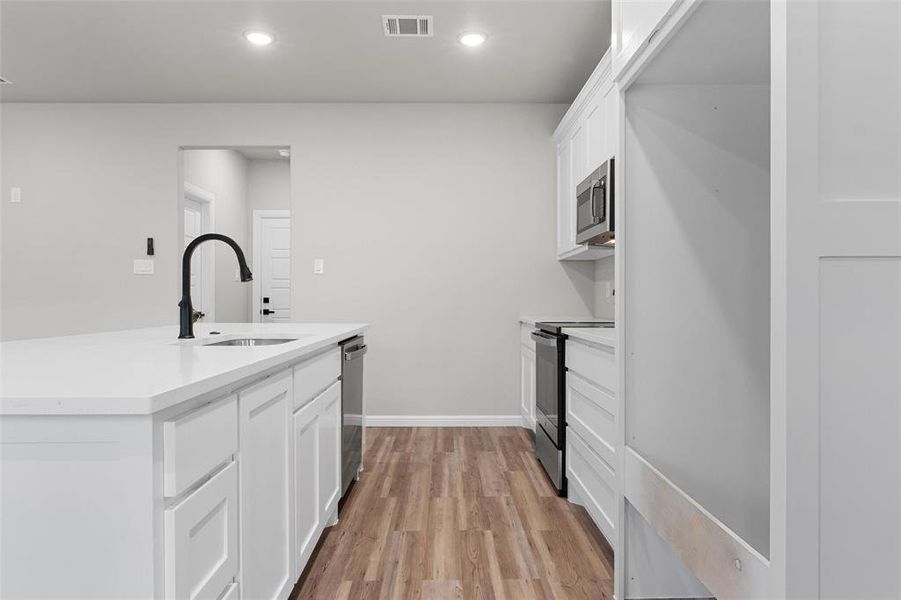 Kitchen with white cabinetry, light wood-style floors, a kitchen island with sink, recessed lighting, and stainless steel appliances Kitchen with white cabinetry, light wood-style floors, a kitchen island with sink, recessed lighting, and stainless steel appliances