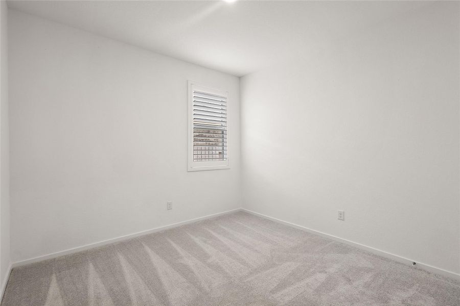 This photo shows a bright, small room with clean white walls and a light gray carpet. A window with shutters allows natural light to enter, creating a cozy atmosphere. Ideal for a home office or small bedroom.