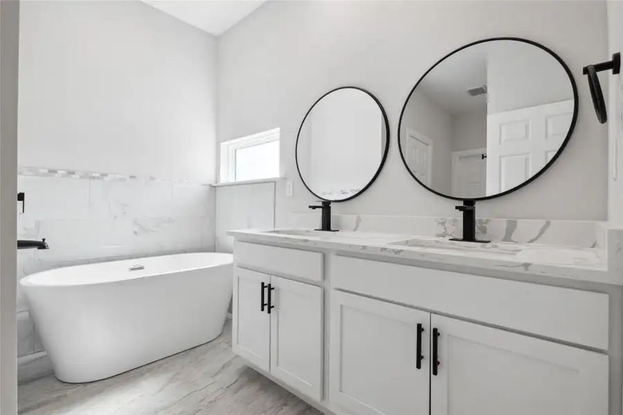 Full bathroom featuring double vanity, a freestanding tub, tile walls, a wainscoted wall, and marble finish flooring Full bathroom featuring double vanity, a freestanding tub, tile walls, a wainscoted wall, and marble finish flooring
