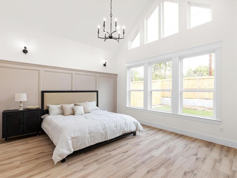 Bedroom with high vaulted ceiling, light wood-style floors, a decorative wall, and a chandelier