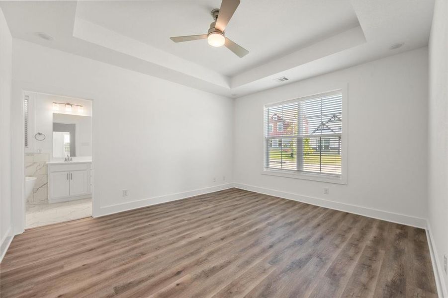 Primary bedroom with a raised ceiling, multiple windows, ensuite bath, LVP flooring. ceiling fan & large walk-in closet.