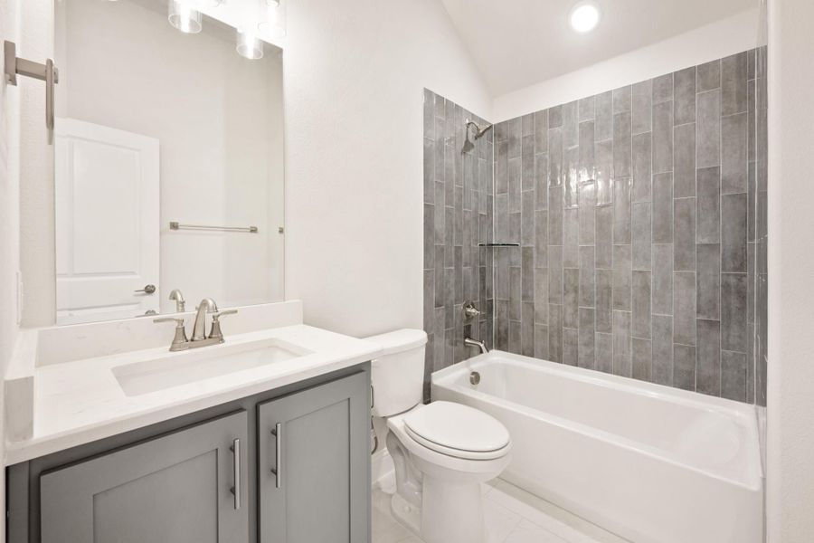 Bathroom with gray vanity, white countertop, and tub-shower combo with gray tile surround
