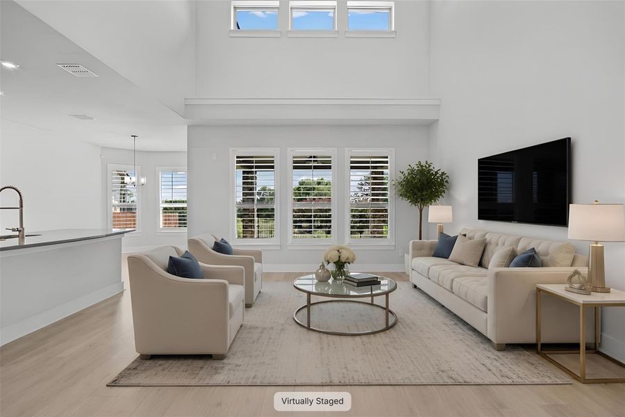An airy living room with high ceilings flows into an open-concept kitchen, all bathed in natural light.