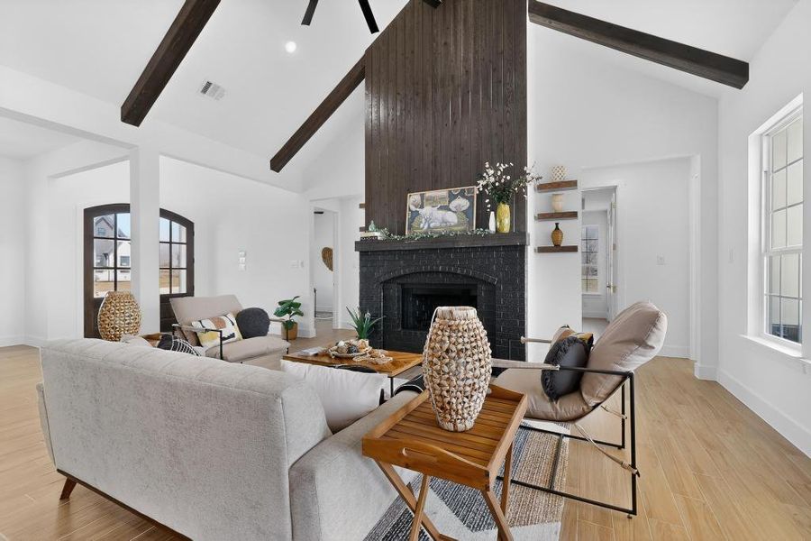 Living area with light wood finished floors, a brick fireplace, a ceiling fan, and vaulted ceiling