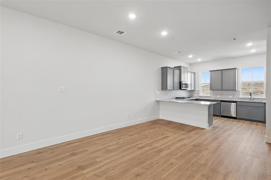 Kitchen with a peninsula, gray cabinets, decorative backsplash, light wood-type flooring, and stainless steel appliances