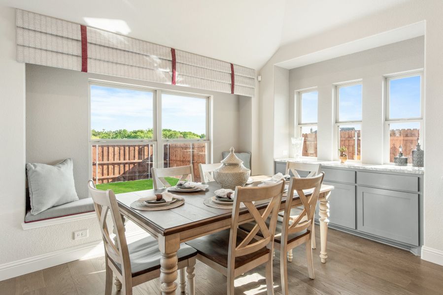 Bright dining area with wood table, built-in window seat, and hardwood floors overlooking a fenced backyard