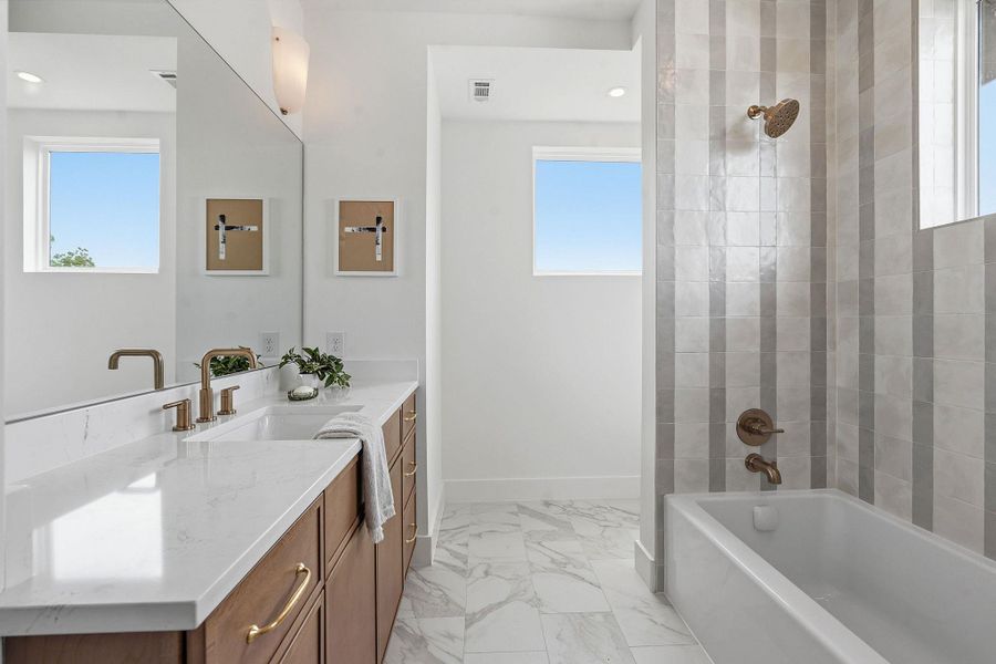 Contemporary bathroom featuring a long wood-finish vanity with a white countertop and dual sinks, complemented by brass-finish fixtures