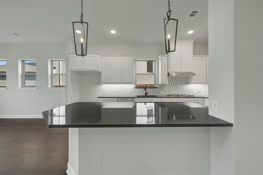 Kitchen featuring tasteful backsplash, a breakfast bar area, white cabinets, dark wood-style floors, and a peninsula