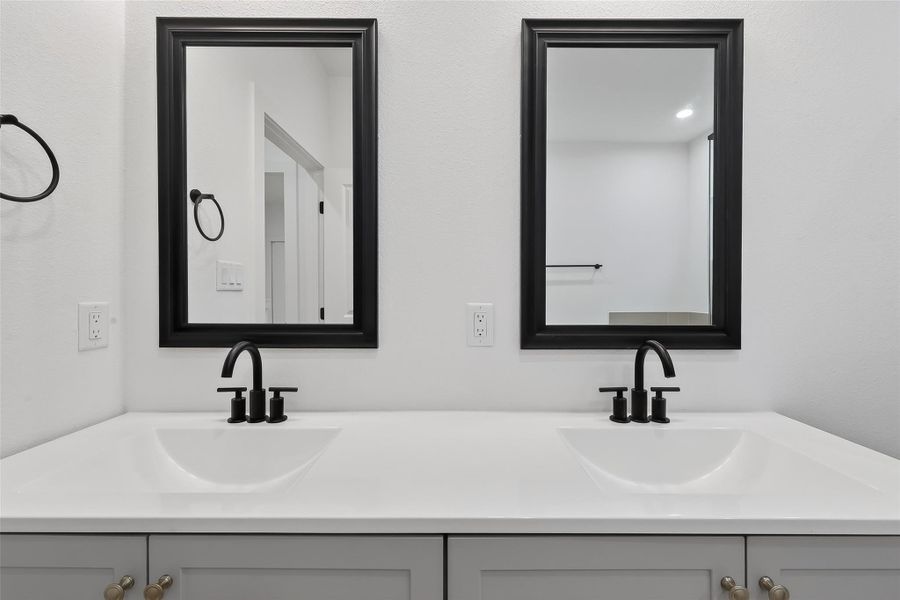 This bathroom features a modern double vanity with sleek black faucets and framed mirrors, offering a clean, stylish look.
