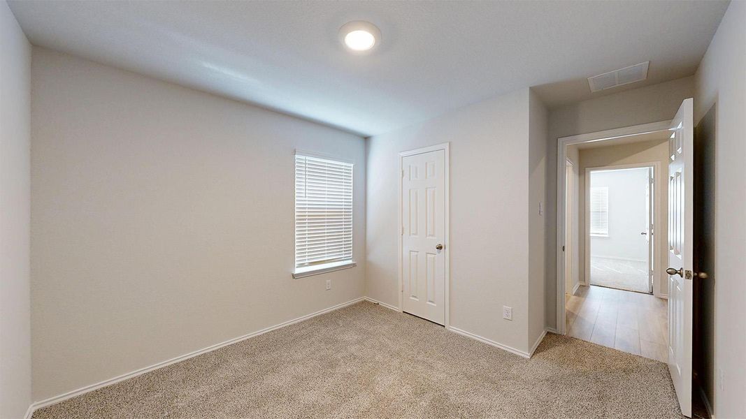 A well-lit bedroom features plush carpeting and a practical window with blinds.