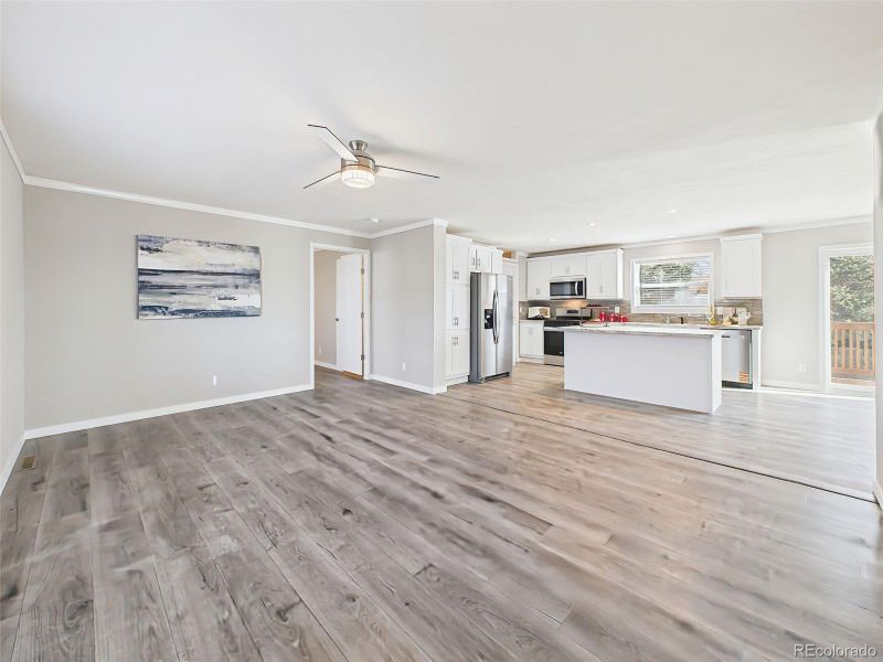 Family Room with Kitchen View (Unstaged) – Clean lines and open flow continue with ample natural light and views into the bright white kitchen with island seating.