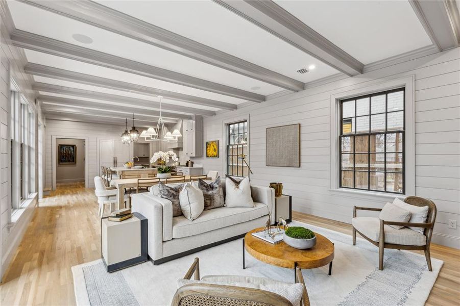 Living room featuring beam ceiling, crown molding, a notable chandelier, light wood-type flooring, and baseboards