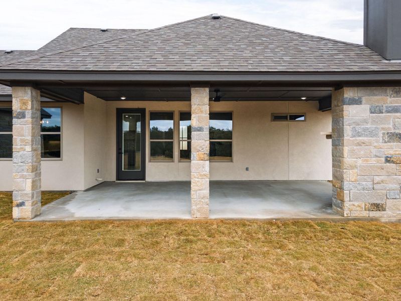 Rear view of property with a shingled roof, a patio, a yard, and stone siding