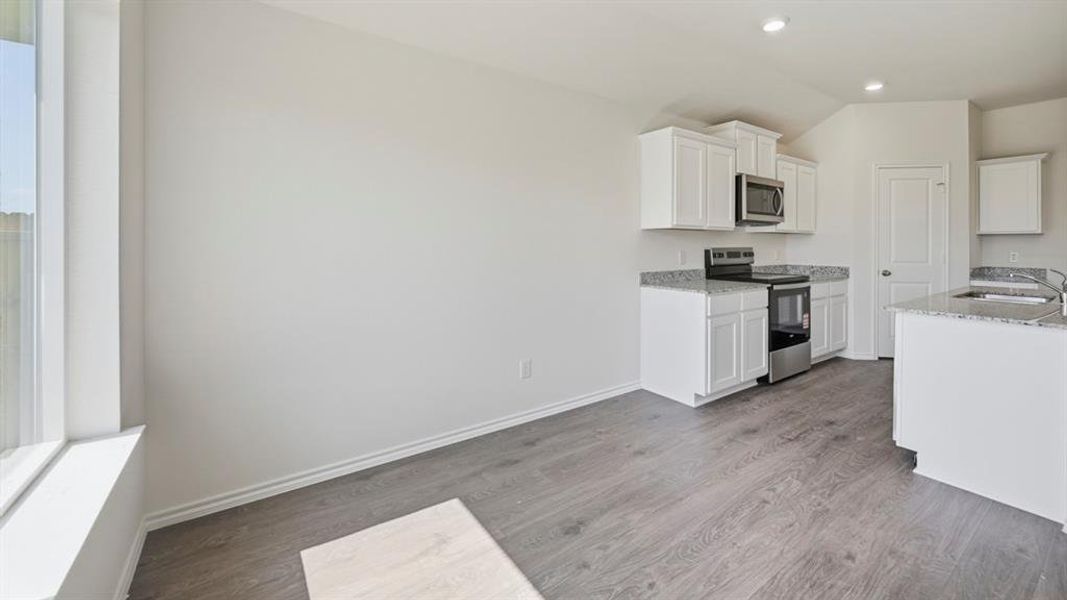 Kitchen featuring white cabinets, stainless steel appliances, light stone countertops, dark wood-style flooring, and lofted ceiling