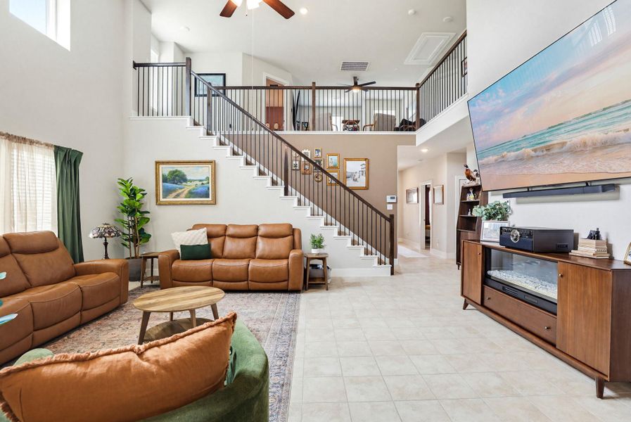 Open-concept living space with a double-height ceiling, ceramic tile flooring, and a prominent staircase featuring dark wood handrails and black metal balusters