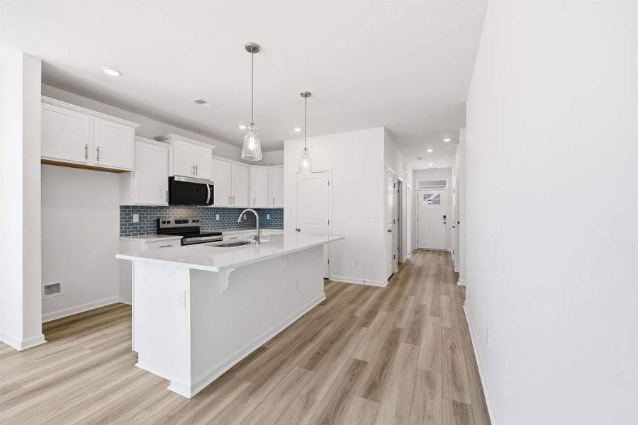 Kitchen featuring hanging light fixtures, white cabinets, stainless steel appliances, a breakfast bar area, and a center island with sink Kitchen featuring hanging light fixtures, white cabinets, stainless steel appliances, a breakfast bar area, and a center island with sink